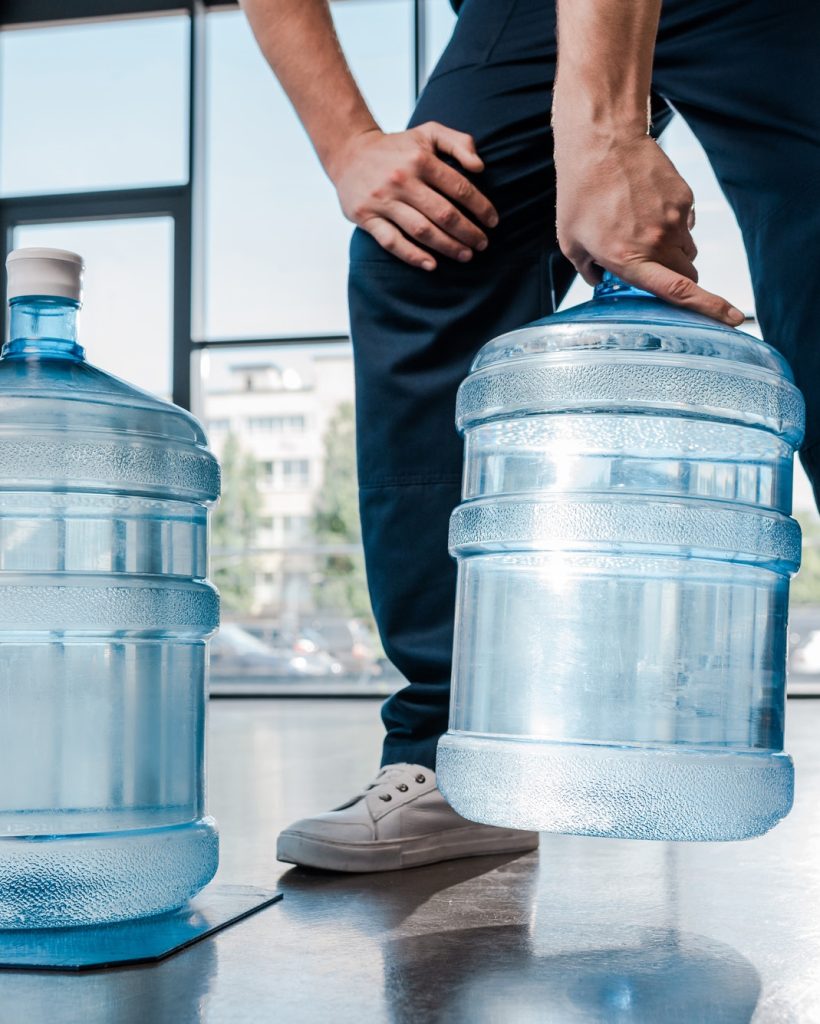 cropped-view-of-delivery-man-holding-heavy-bottle-with-water-near-hand-truck.jpg